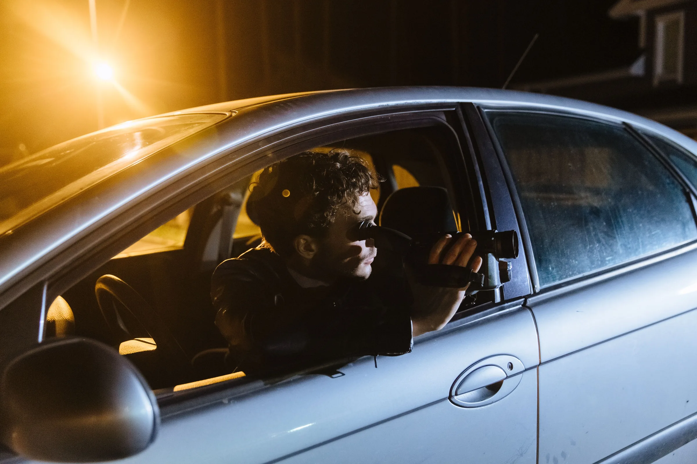 Private investigator photographing from inside a vehicle with a professional camera.